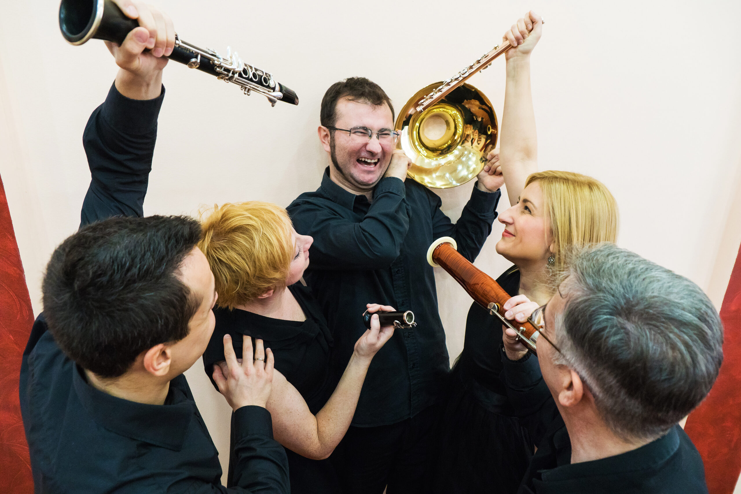 novosadski duvački kvintet, na slici nekoliko muzičara drži svoje instrumente prema jednom koji stoji u centru i jako se smeje svojim kolegama