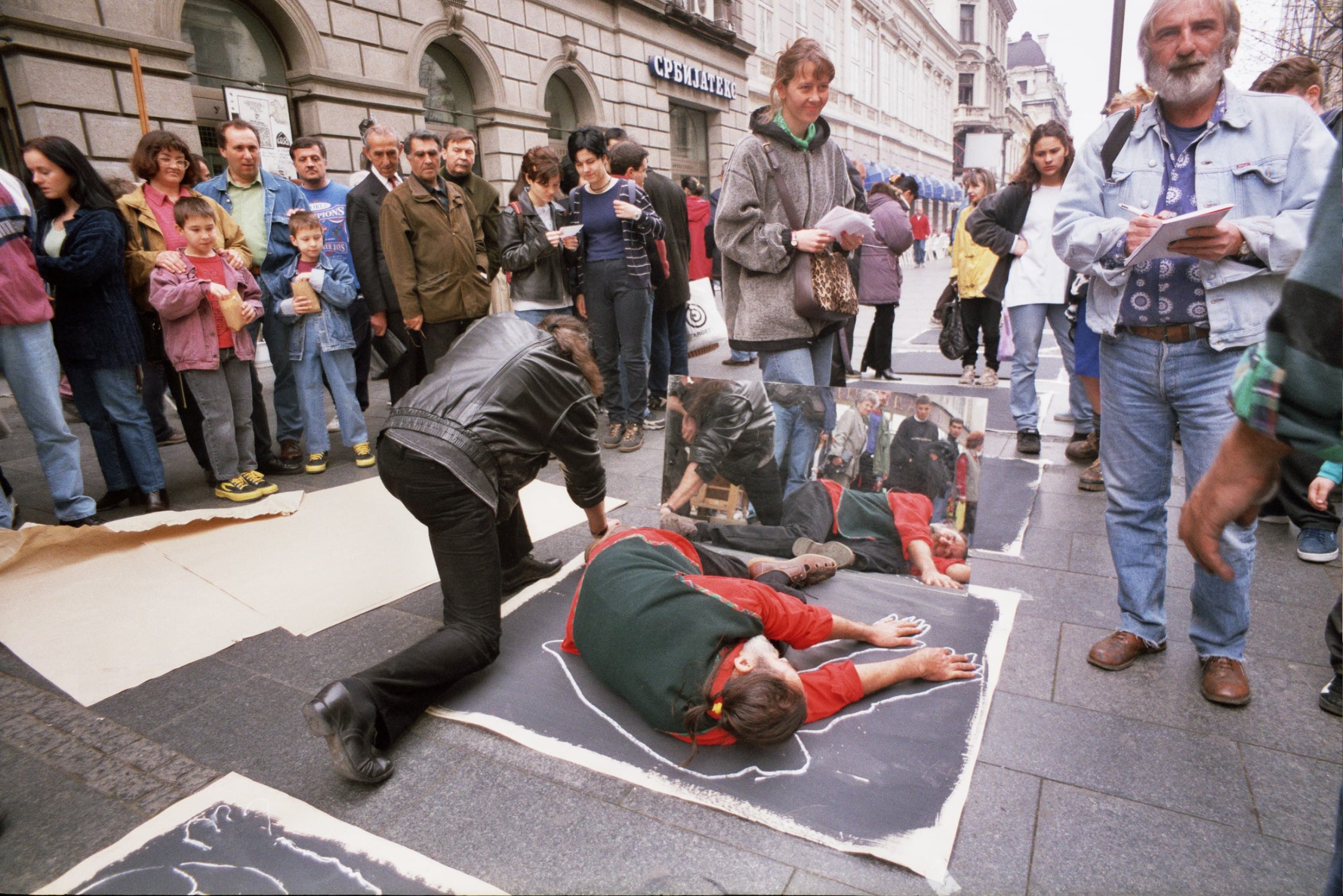 Performans rekonstrukcije zločina gde su na ulici ljudi koji leže na crnom papiru i oko njih opcrtavaju belom kredom