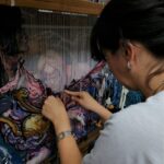 Ženska nit - žena koja radi tapiseriju na kojoj se vidi deo rada na kojem je super-heroj