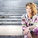 Andrea Popov, umetnica, u šarenoj letnjoj haljini, sedi na stepenicama